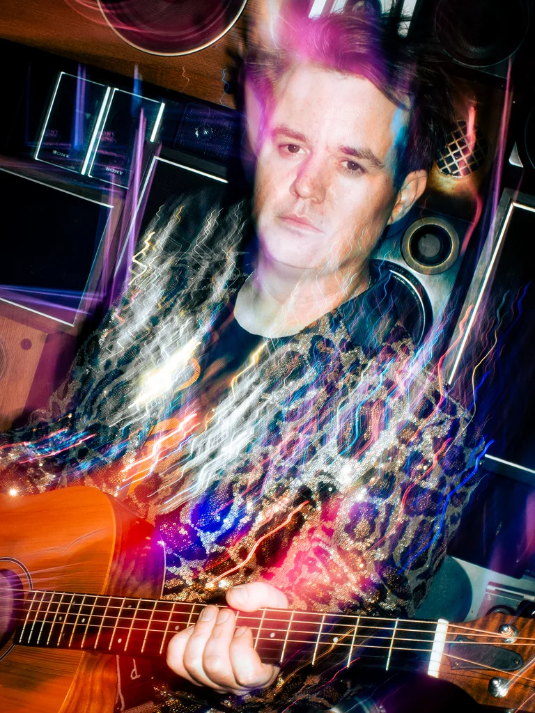 Ben Hawes with his guitar under warm stage lights